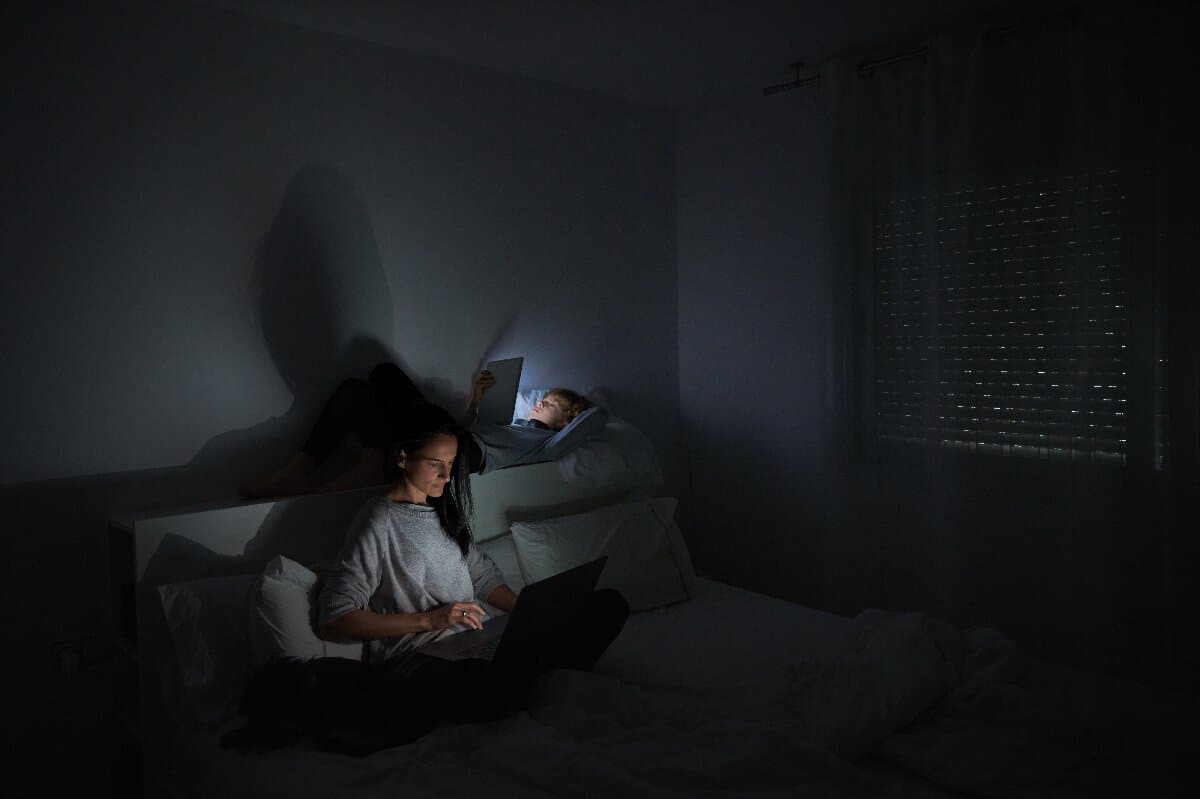 mother-and-son-using-gadgets-in-bedroom-at-night